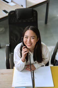 Smiling woman in office taking a phone call, conveying professionalism and friendliness.